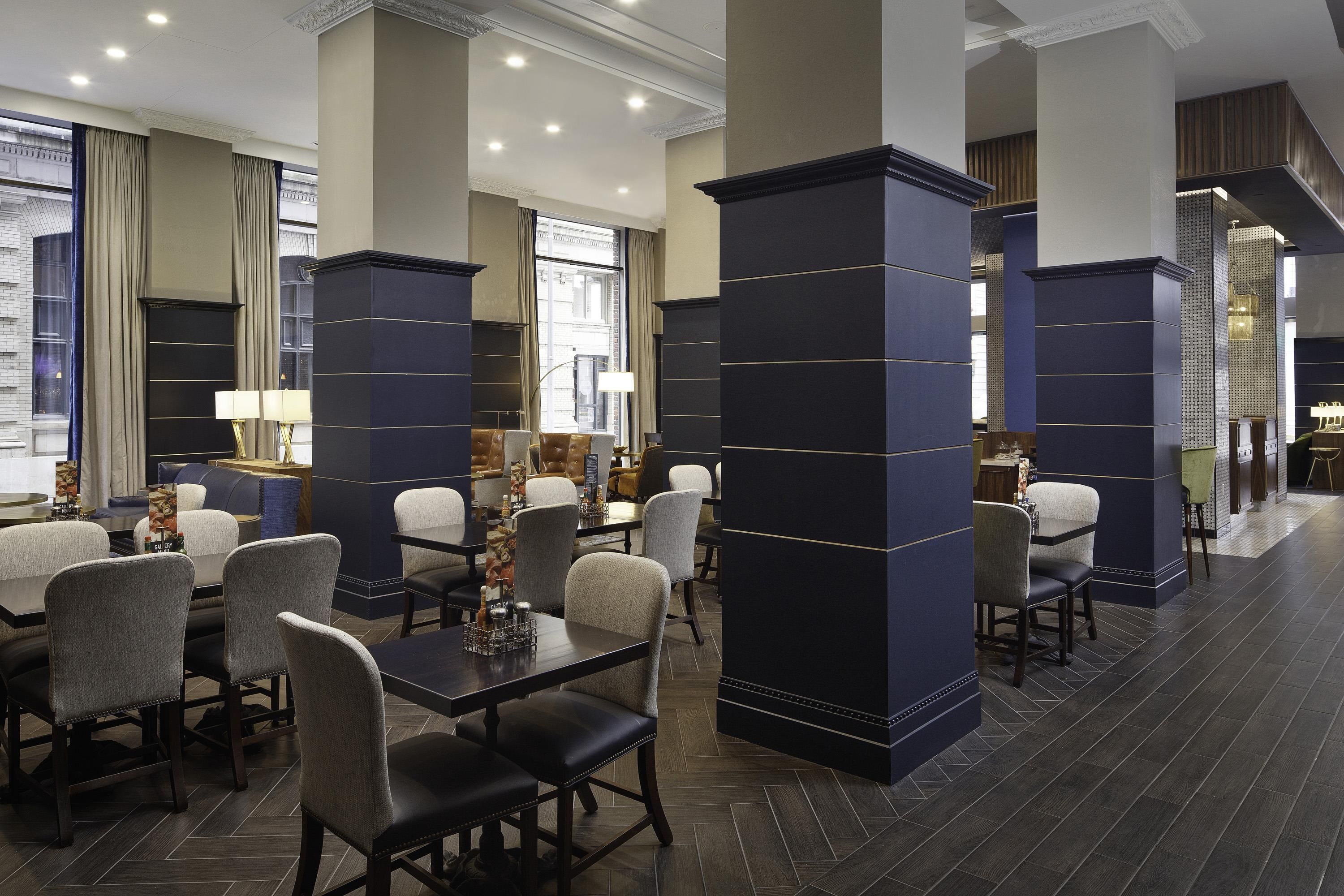 A modern hotel lobby with dark blue pillars, comfortable seating, and large windows offering views of the city.