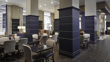 A modern hotel lobby with dark blue pillars, comfortable seating, and large windows offering views of the city.