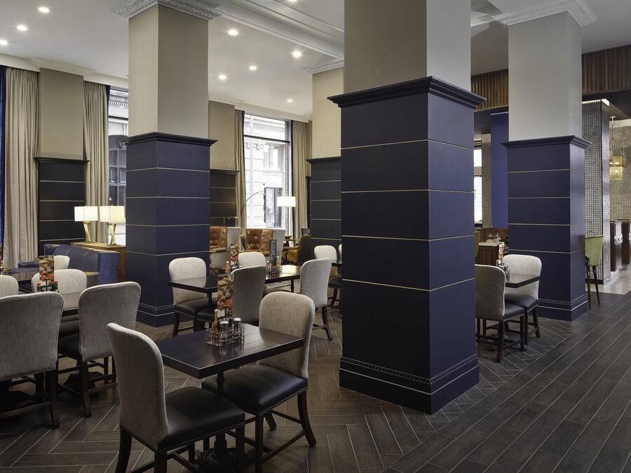 A modern hotel lobby with dark blue pillars, comfortable seating, and large windows offering views of the city.
