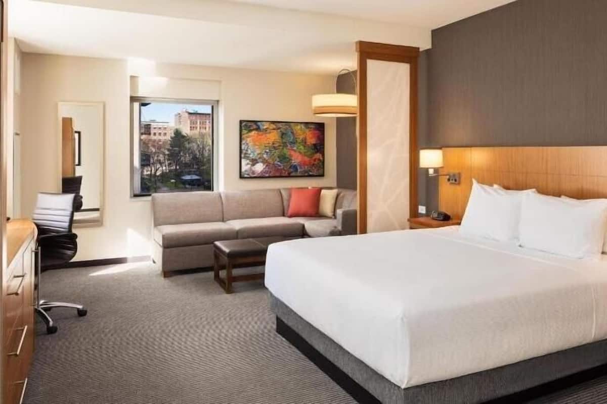 A hotel room with a large bed, a sofa, a desk, and a painting.
