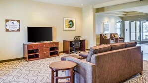 Un hall d’hôtel avec un téléviseur, un bureau, un canapé et un fauteuil.
