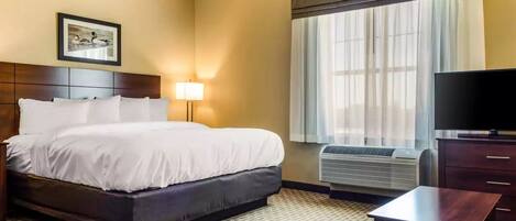 A hotel room with a bed, a television, a desk, and a window with curtains.