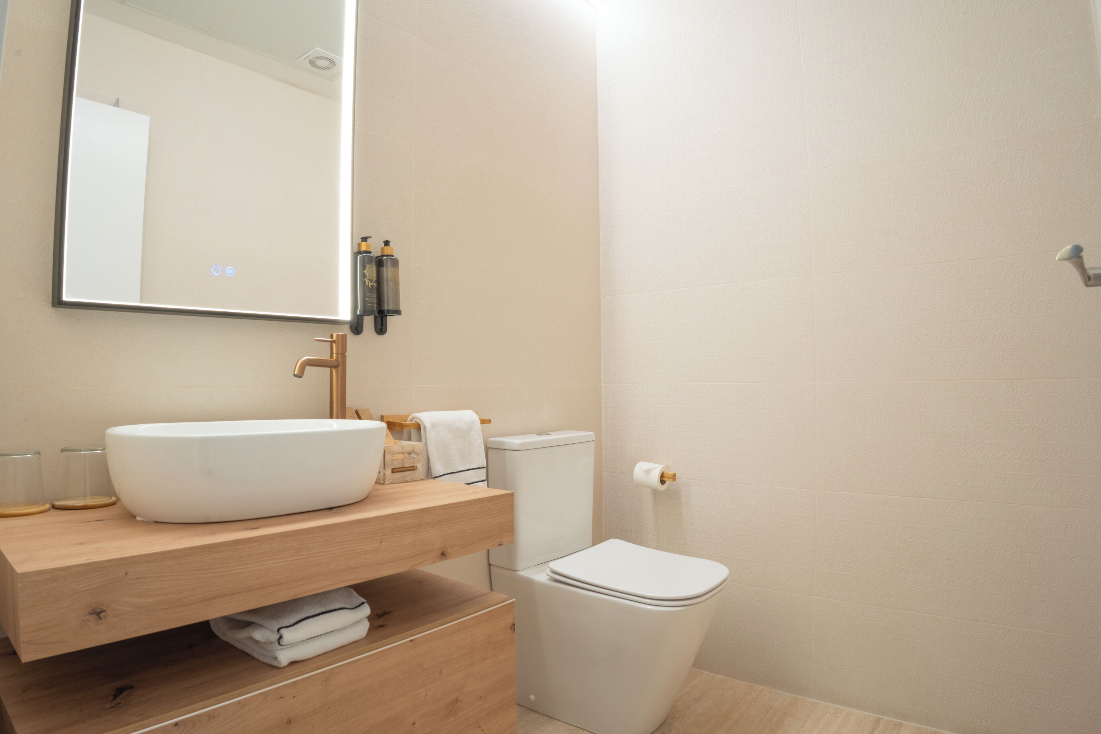 A modern bathroom with a large mirror, a wooden vanity, a white sink, and a toilet.