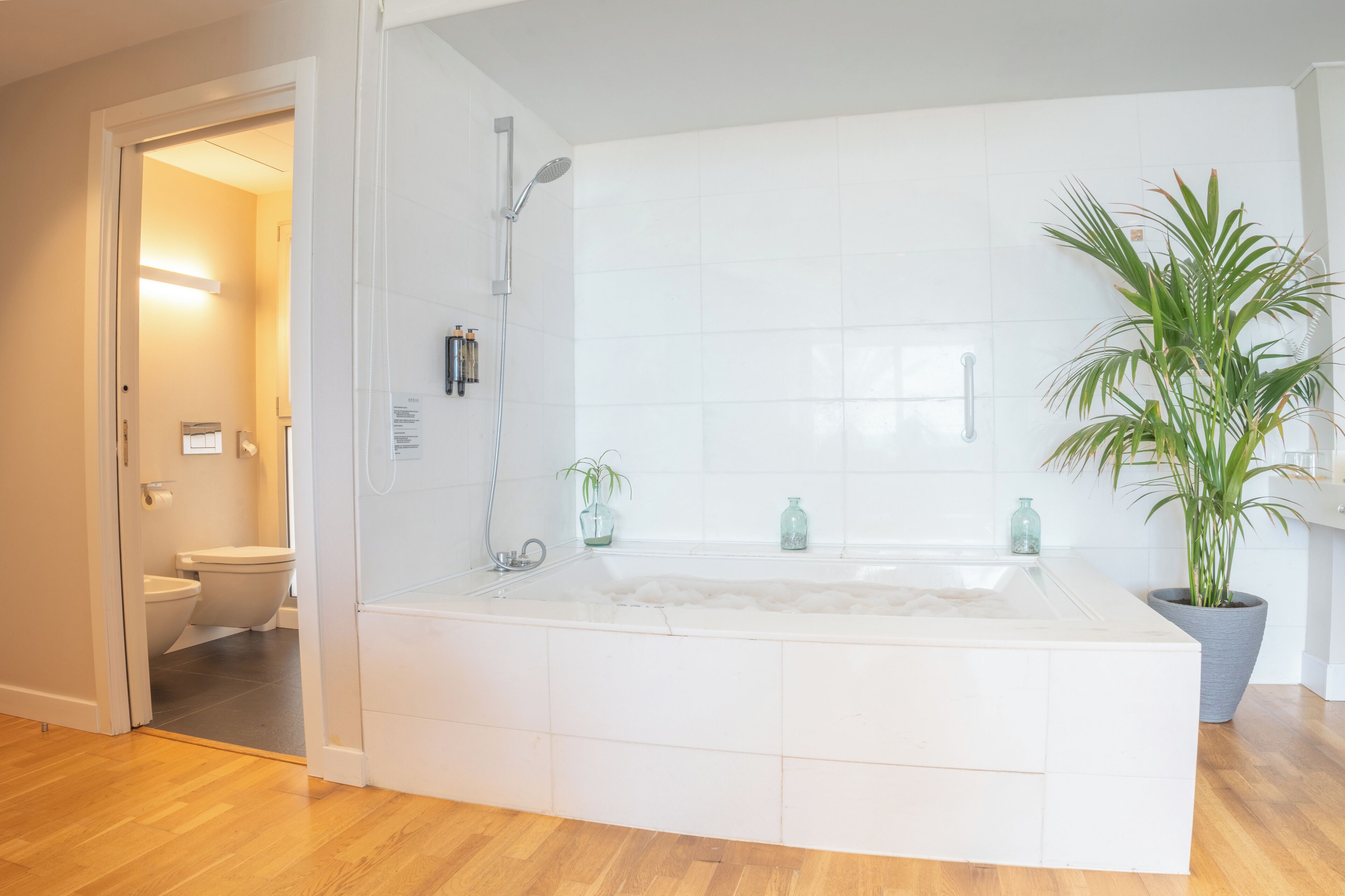 Une salle de bain moderne avec une grande baignoire, une douche et des toilettes. On y trouve des plantes en pot et des articles de toilette sur le comptoir du lavabo.