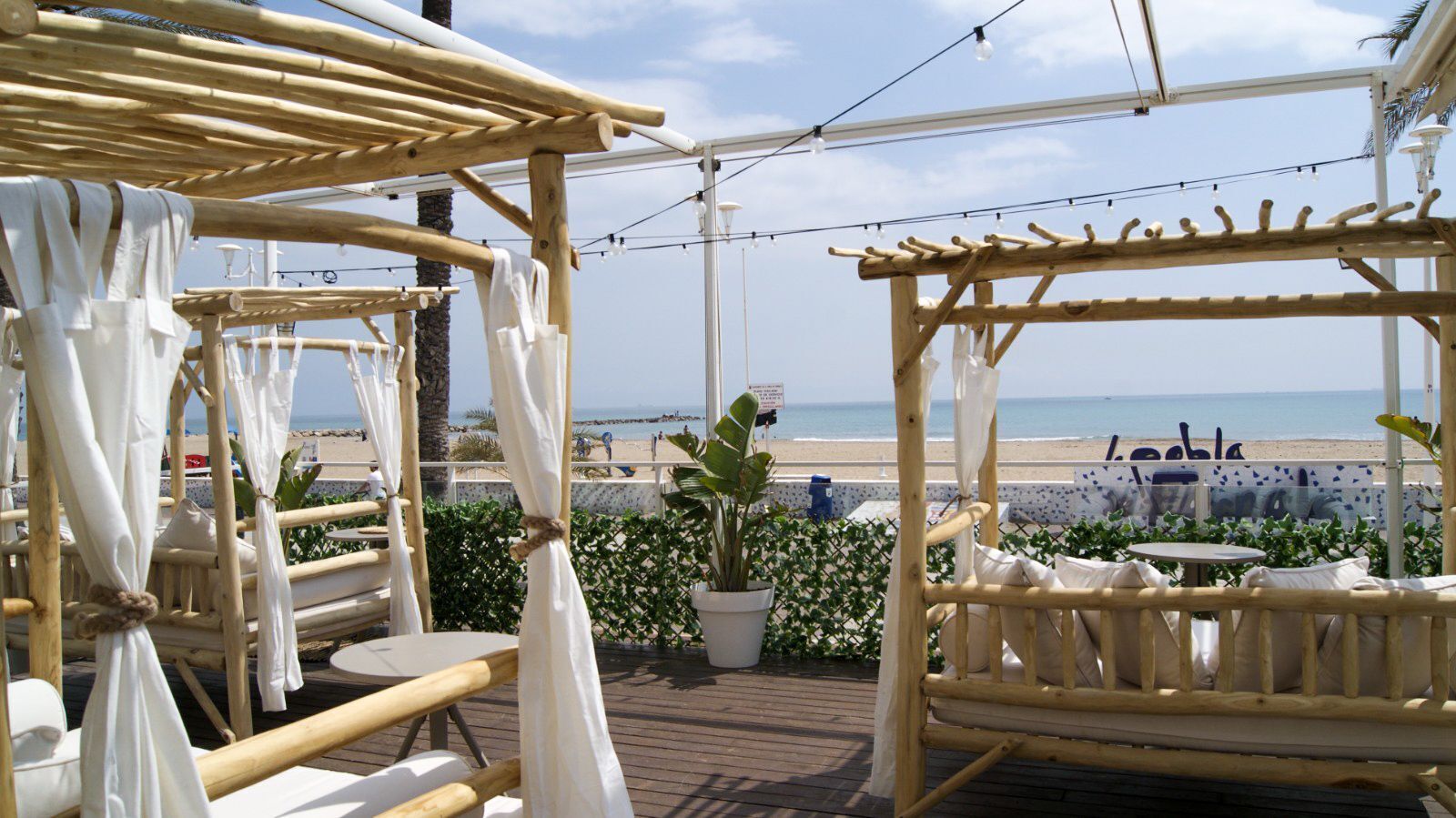 An outdoor seating area with bamboo furniture and white cushions, overlooking a beach.