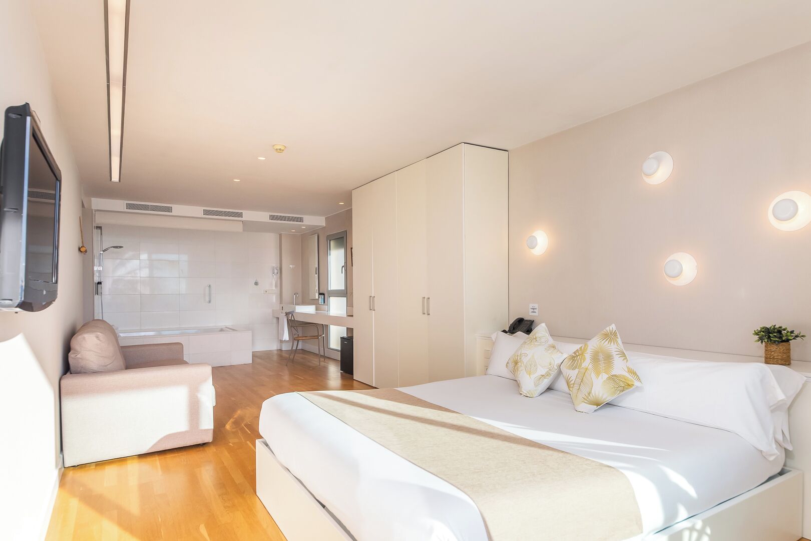 Quarto moderno com cama grande, área de estar e banheiro.