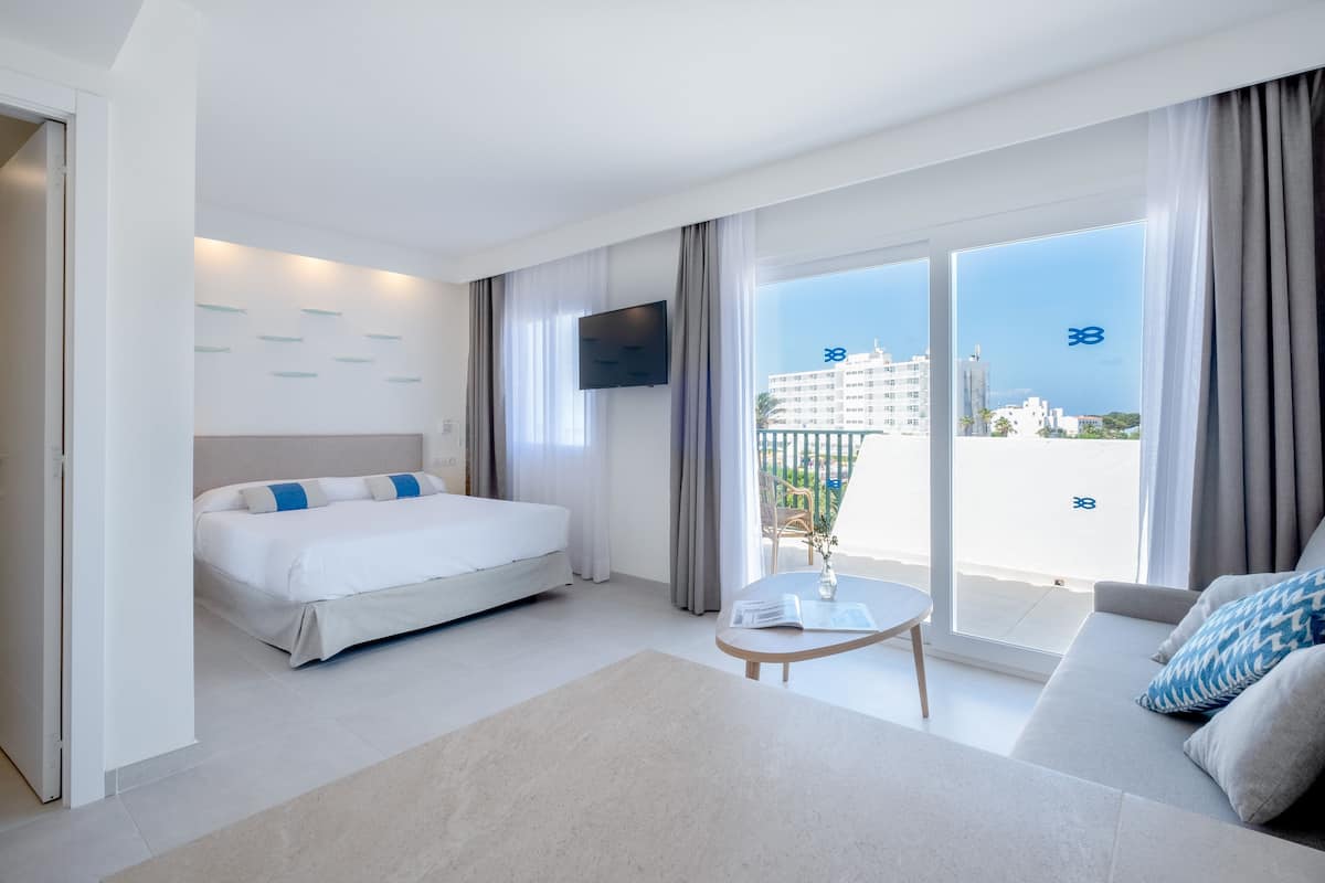 Una habitación de hotel moderna con cama, sofá, televisor y balcón con vista a la ciudad.