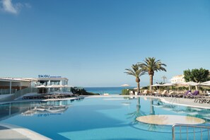 A pool area with lounge chairs and umbrellas, a palm tree, and a building with 'SAIGU' signage. - Fergus Style Carema Beach (Ciutadella de Menorca)