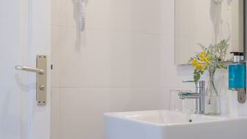 A bathroom with a white sink, a mirror, a hairdryer, and a vase with yellow flowers.