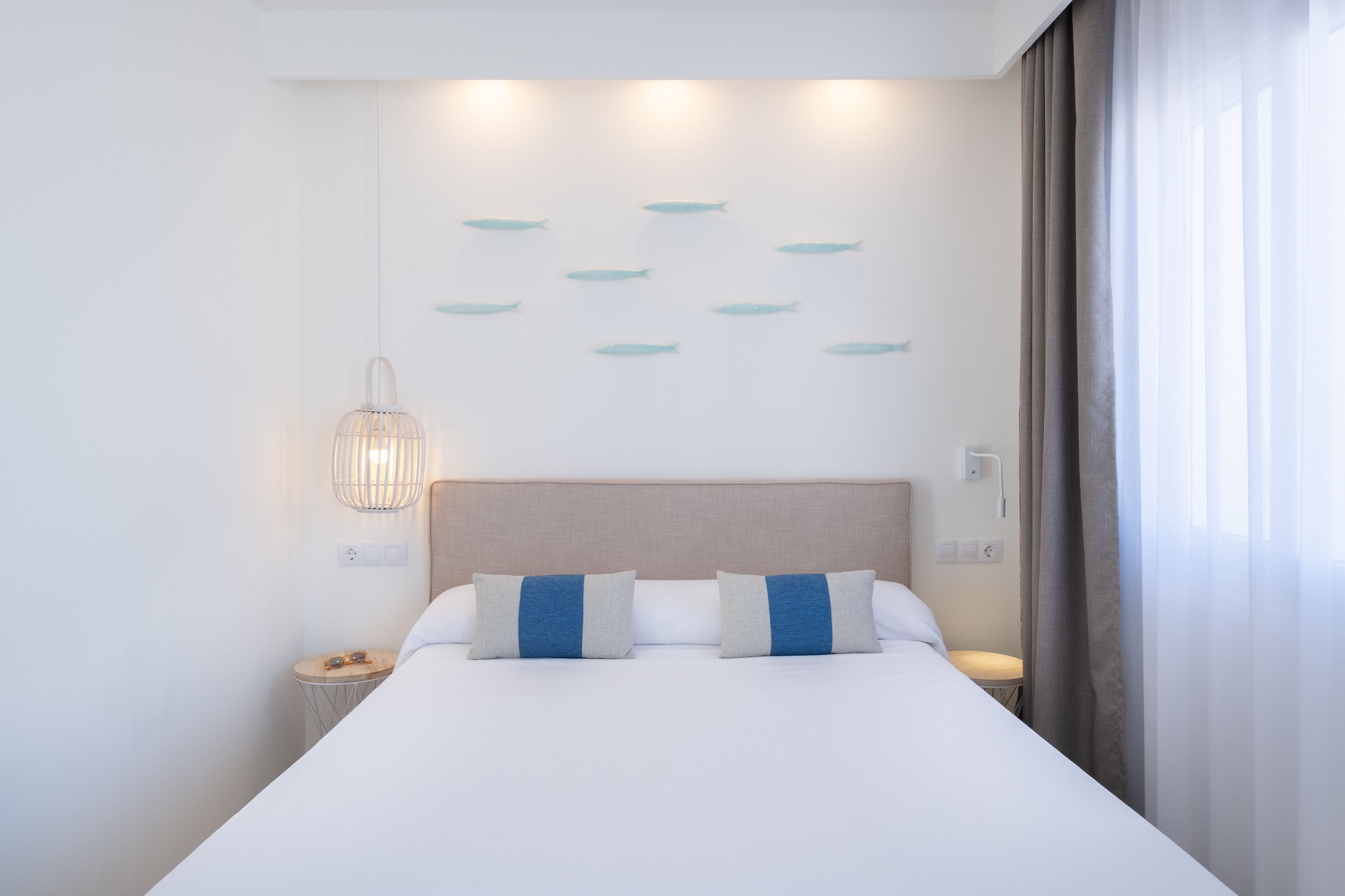 Una habitación de hotel moderna con una cama grande, una mesita de noche, una lámpara de pared y una cortina en la ventana.