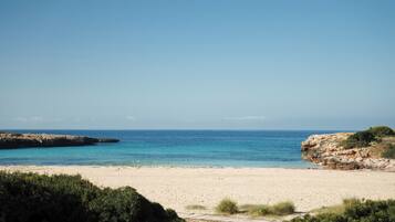 A beach with clear blue water, sandy shore, and rocky cliffs.