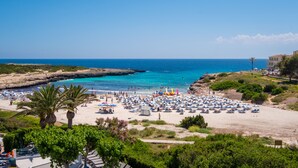 Una platja amb nombrosos paraigües i gandules, mar blava cristal·lina i un litoral rocos.