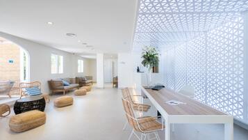 A modern lounge area with wicker furniture, a long table, and a geometric wall design.