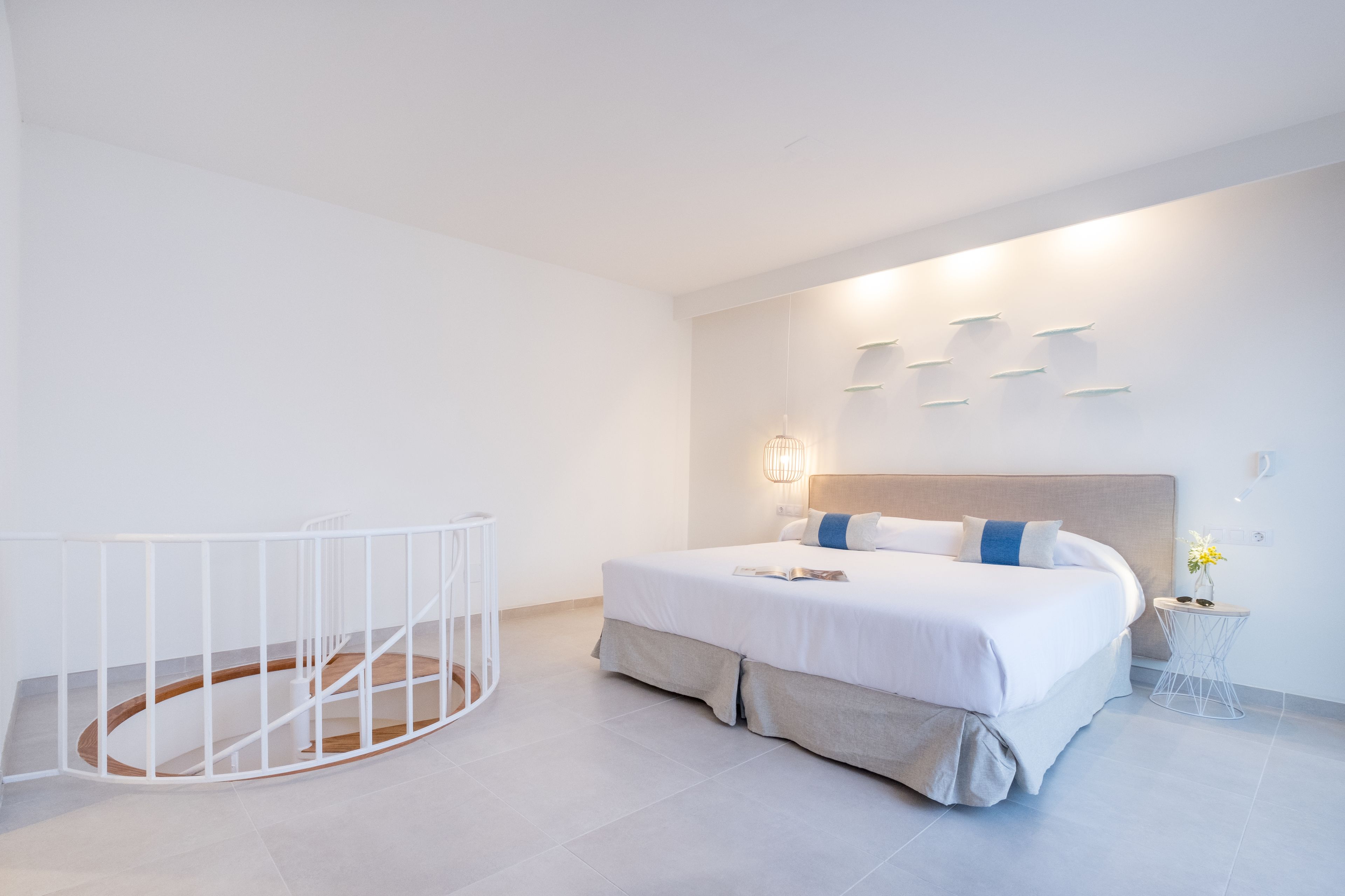 A modern bedroom with a large bed, a white crib, and a wall-mounted light fixture.