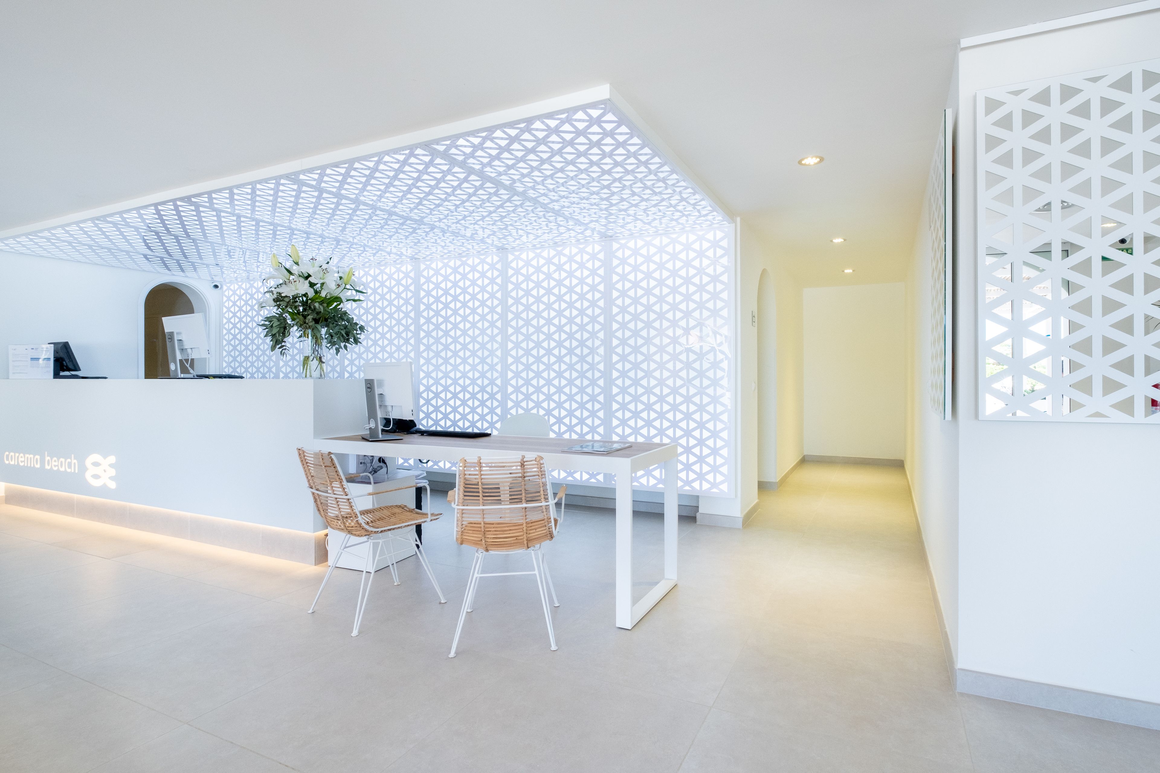 A modern reception area with a white desk, two wicker chairs, and a decorative plant.