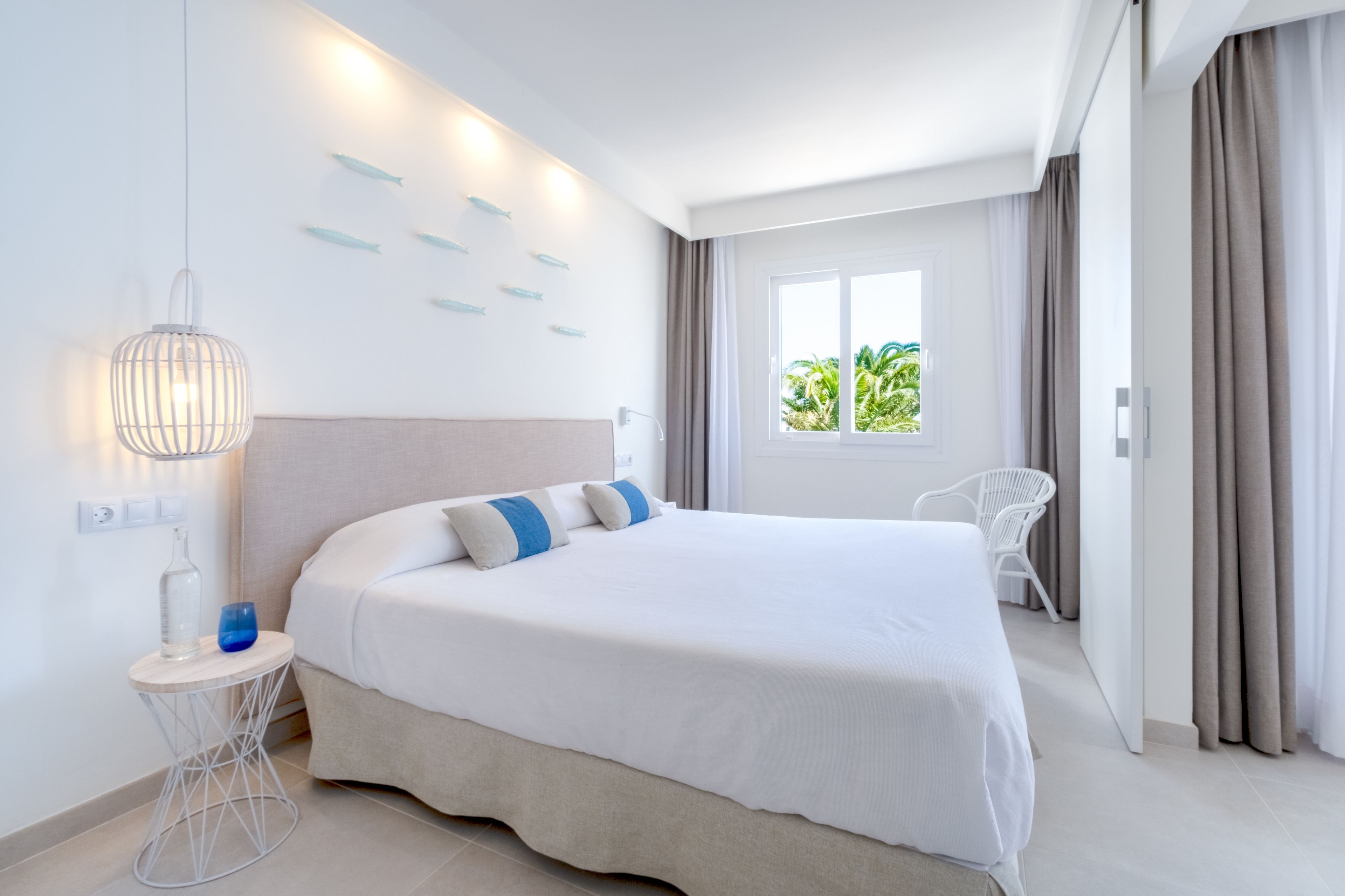 A modern hotel room with a large bed, a bedside table with a lamp, a chair, and a window with curtains.