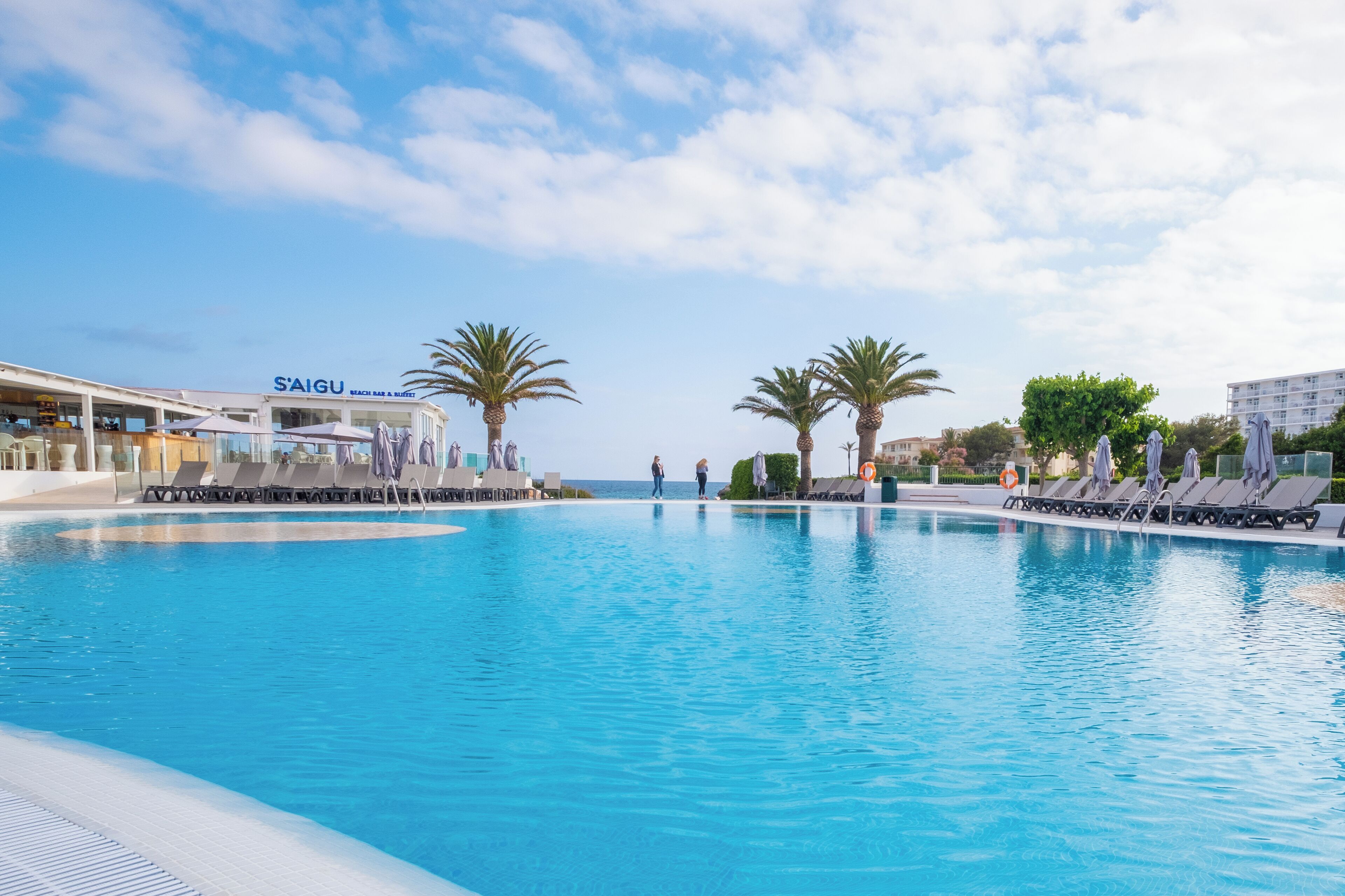A swimming pool with lounge chairs, palm trees, and a beach bar.