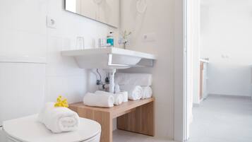 Un baño moderno con inodoro blanco, tocador de madera con lavamanos y toallas dobladas con cuidado.