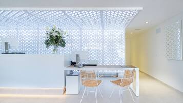 A modern reception area with a white desk, two wicker chairs, a potted plant, and a decorative white lattice ceiling.