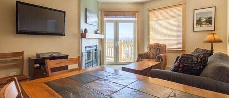 A living room with a stone-tiled table, a sofa, a television, and a balcony with a view.