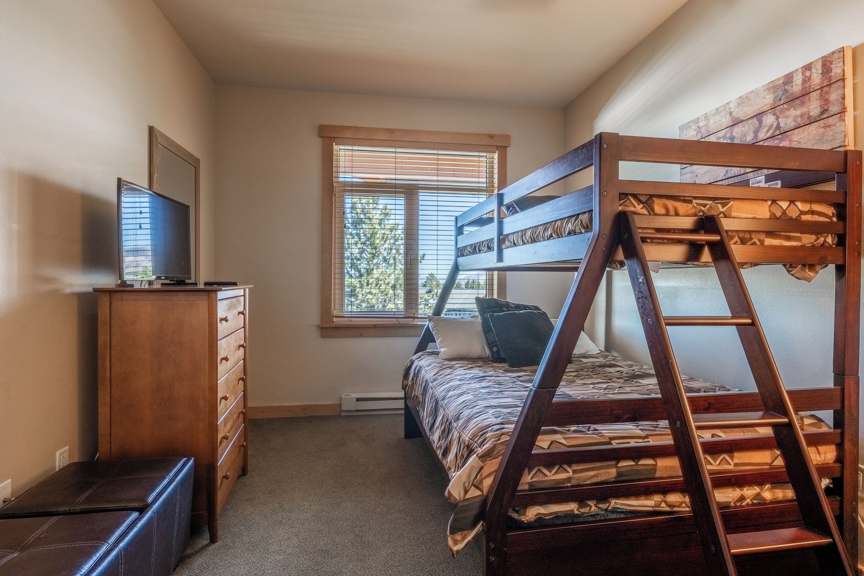 A bedroom with a bunk bed, a dresser, a television, and a window with blinds.