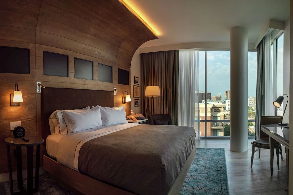 A modern hotel room with a large bed, bedside lamps, a desk, and a view of the city.