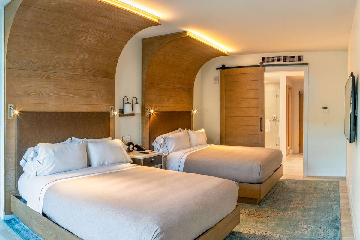 A hotel room with two beds, wooden headboards, and a large arched doorway.