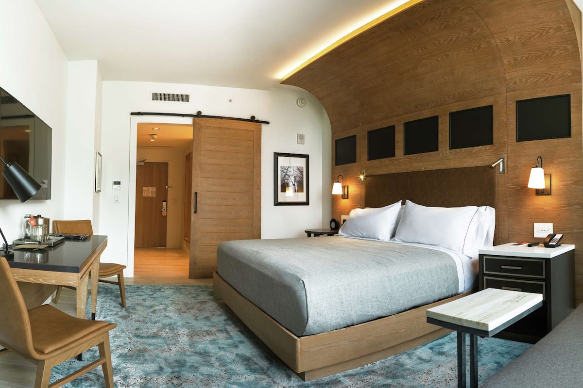 A modern hotel room with a large bed, a desk with a chair, a sofa, and a TV.