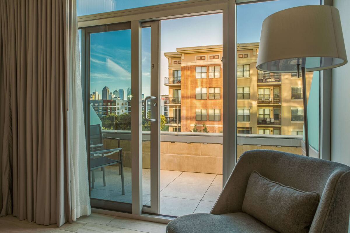 A modern living room with a large sliding glass door leading to a balcony, a grey sofa, and a floor lamp.