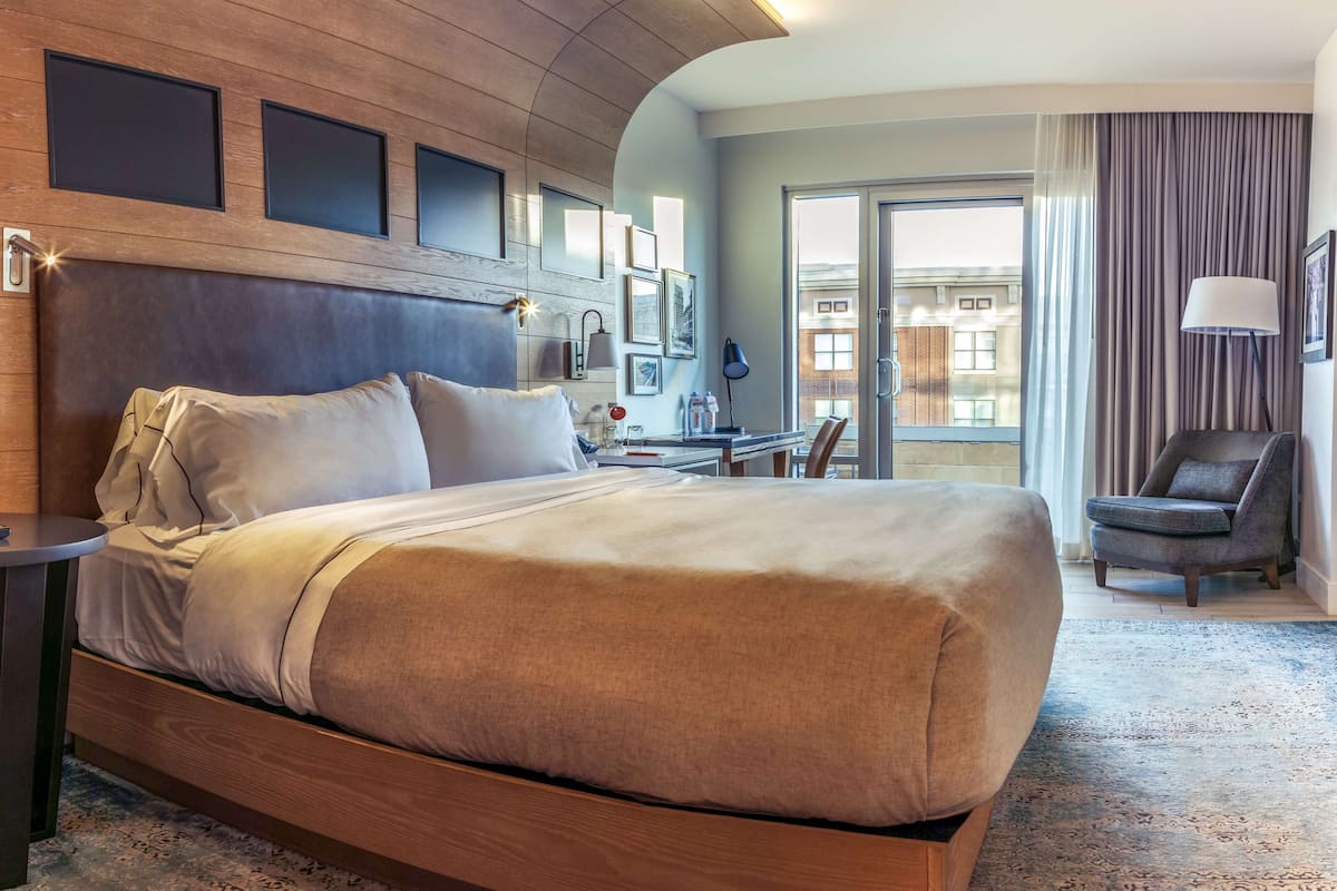 A hotel room with a large bed, a desk, a chair, and a view of the city through the window.