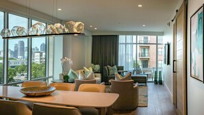 A modern living room with a dining area, large windows, and a city view. - Canopy by Hilton Dallas Uptown (Dallas)