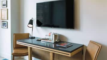 Une chambre moderne dotée d’un téléviseur à écran plat fixé au mur, d’un bureau en bois avec deux chaises, d’une machine à café et d’un magazine.