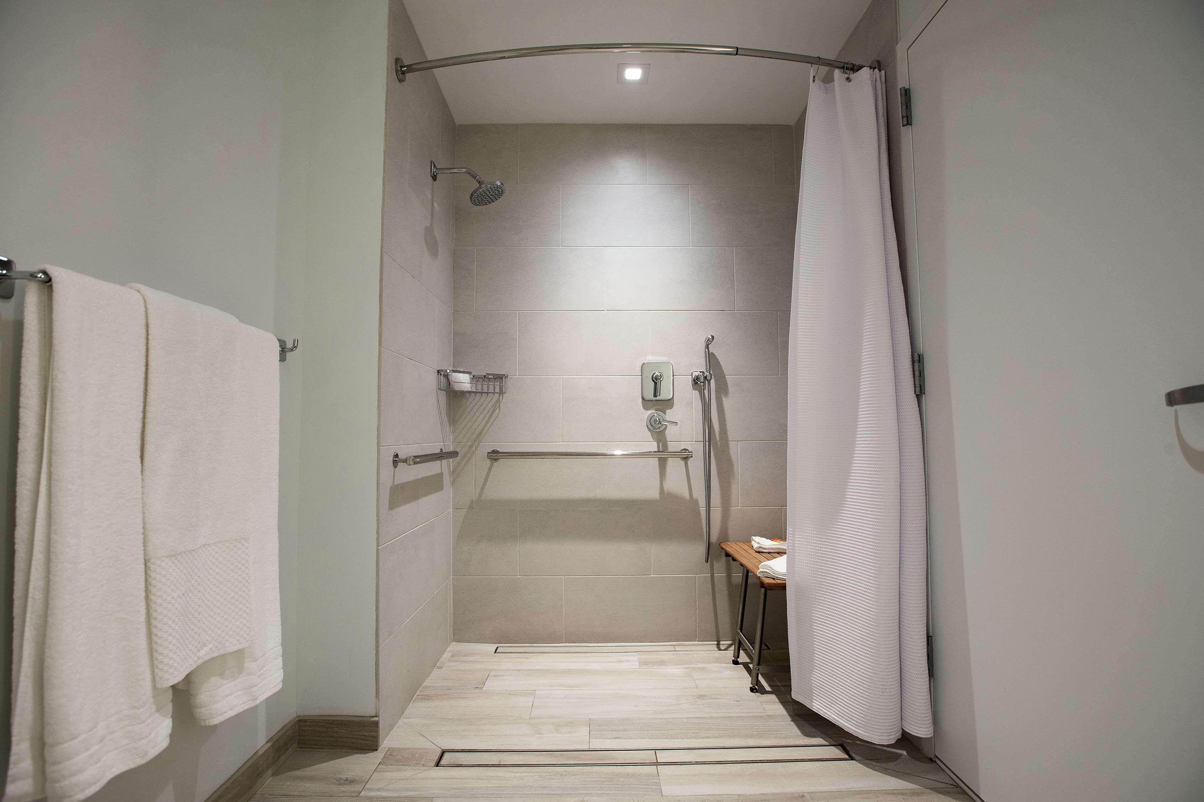 A modern shower area with a grab bar, a towel rack, and a showerhead.
