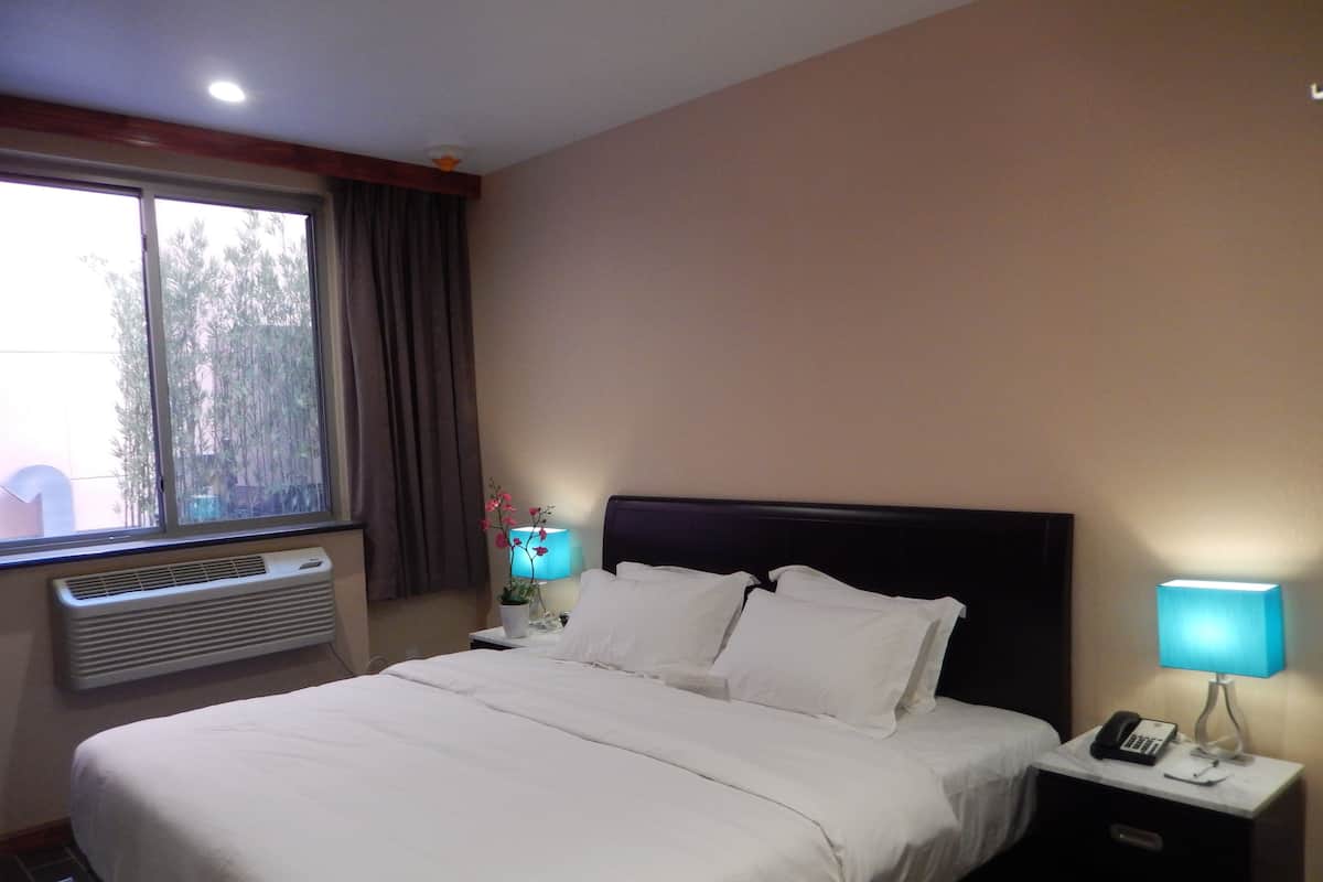 A hotel room with a large bed, a bedside table with a lamp, a phone, and a window with curtains.