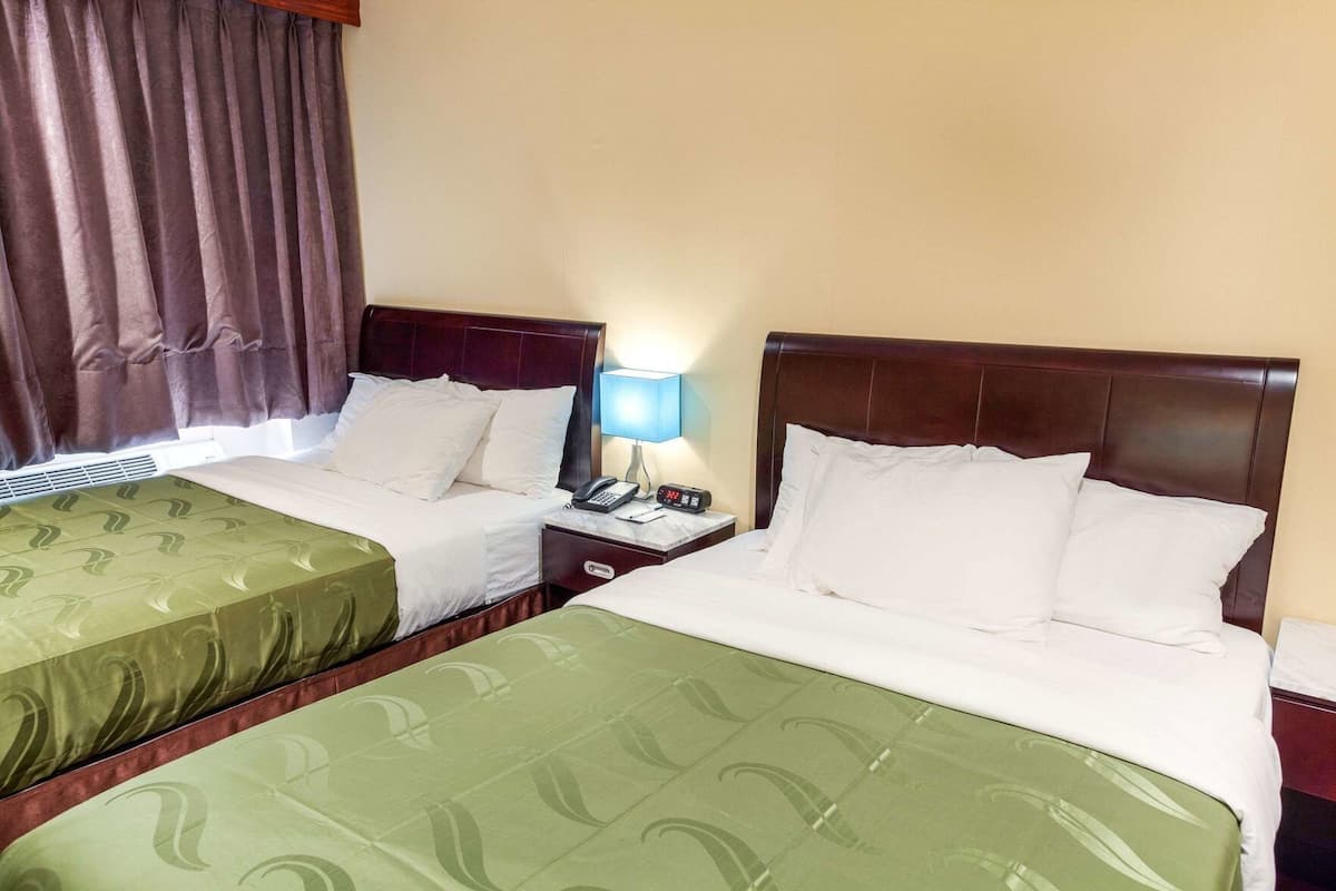 A hotel room with two beds, a nightstand with a lamp, and a window with curtains.