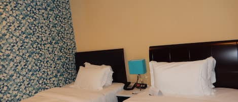 Una habitación de hotel con dos camas, una mesita de noche con lámpara y un papel tapiz estampado.
