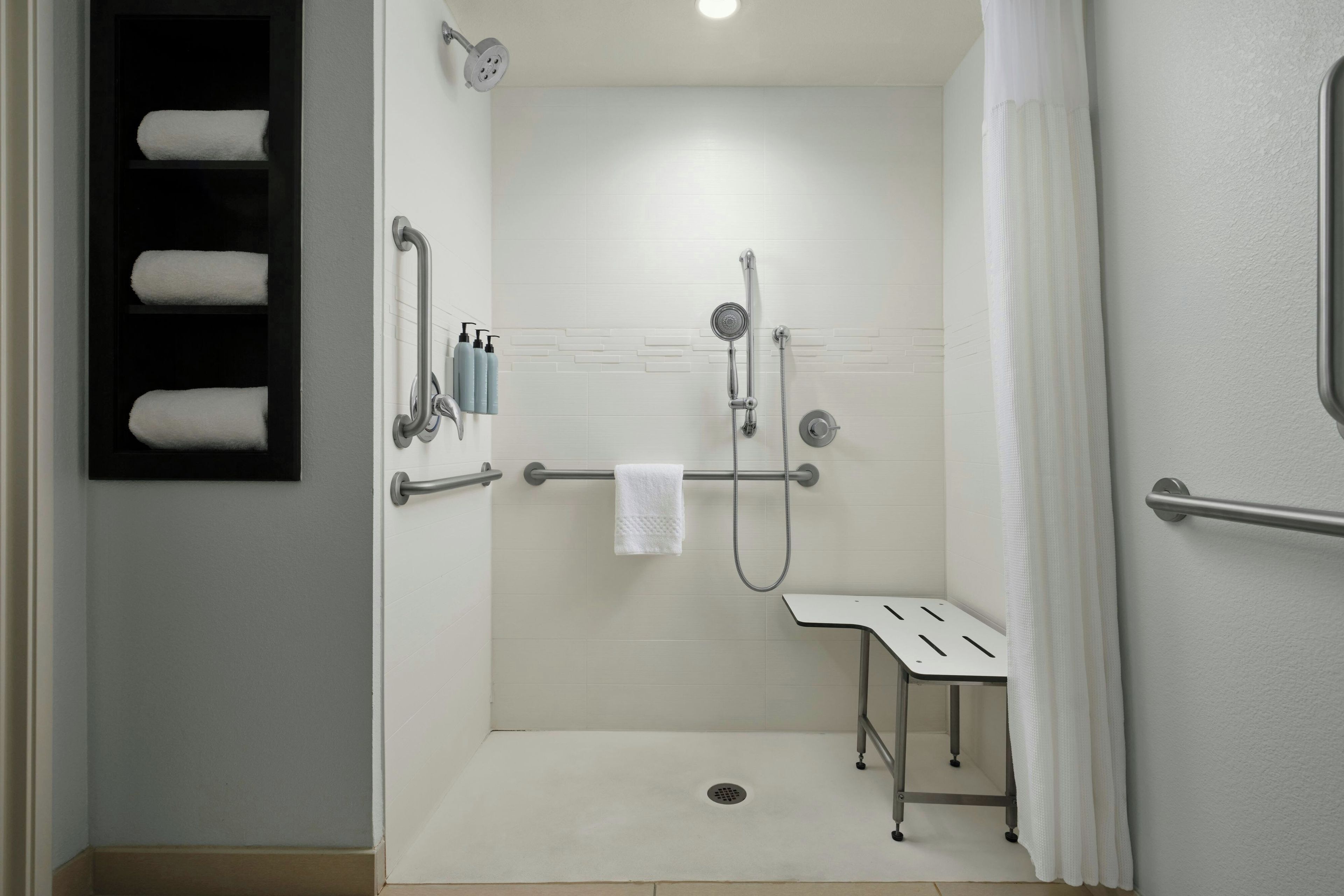 A modern bathroom with a shower, a handrail, and a bench.