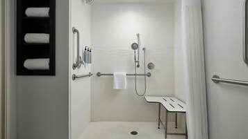 A modern bathroom with a shower, a handrail, and a bench.