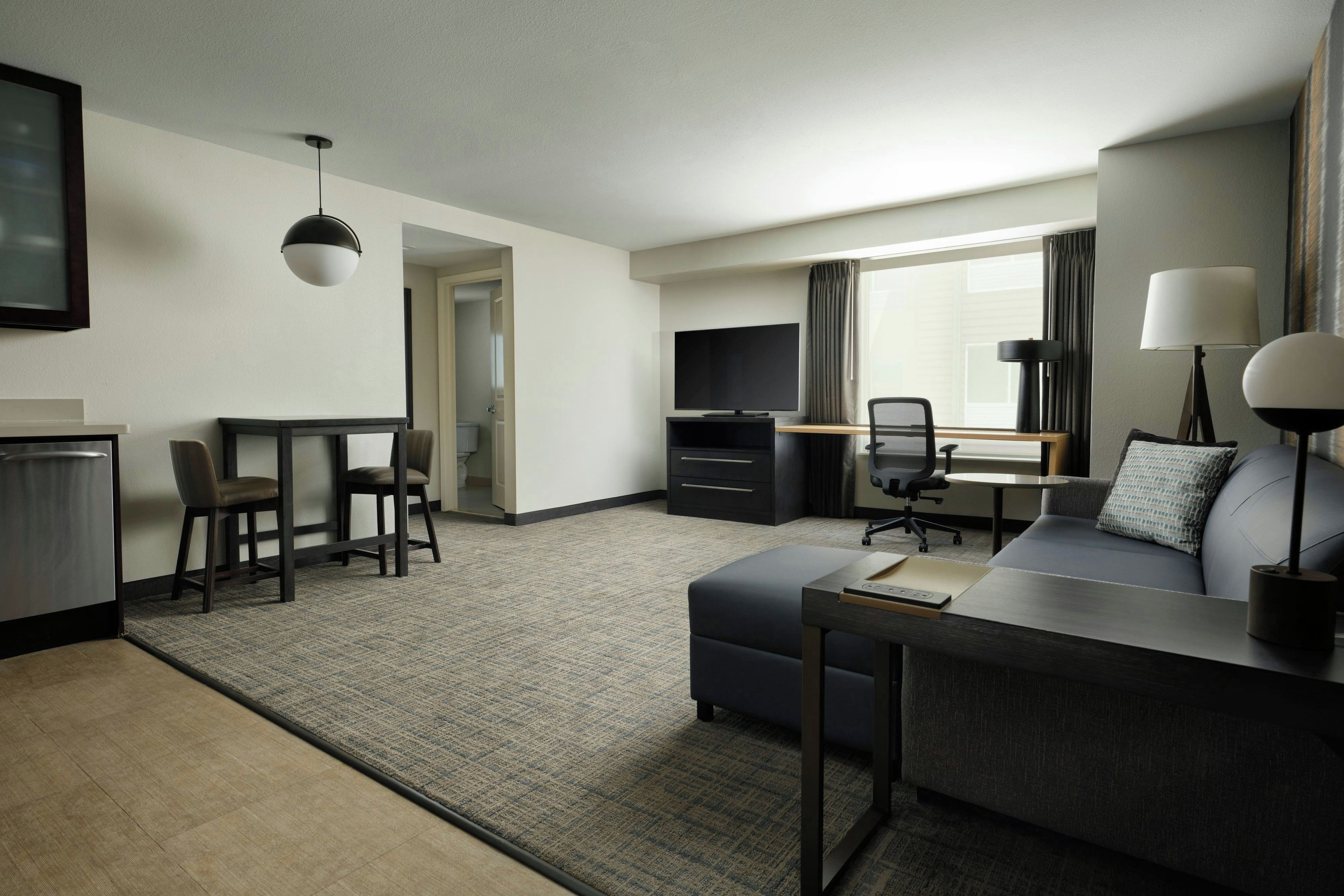 Et moderne hotelværelse med sofa, skrivebord, fjernsyn og spiseplads.