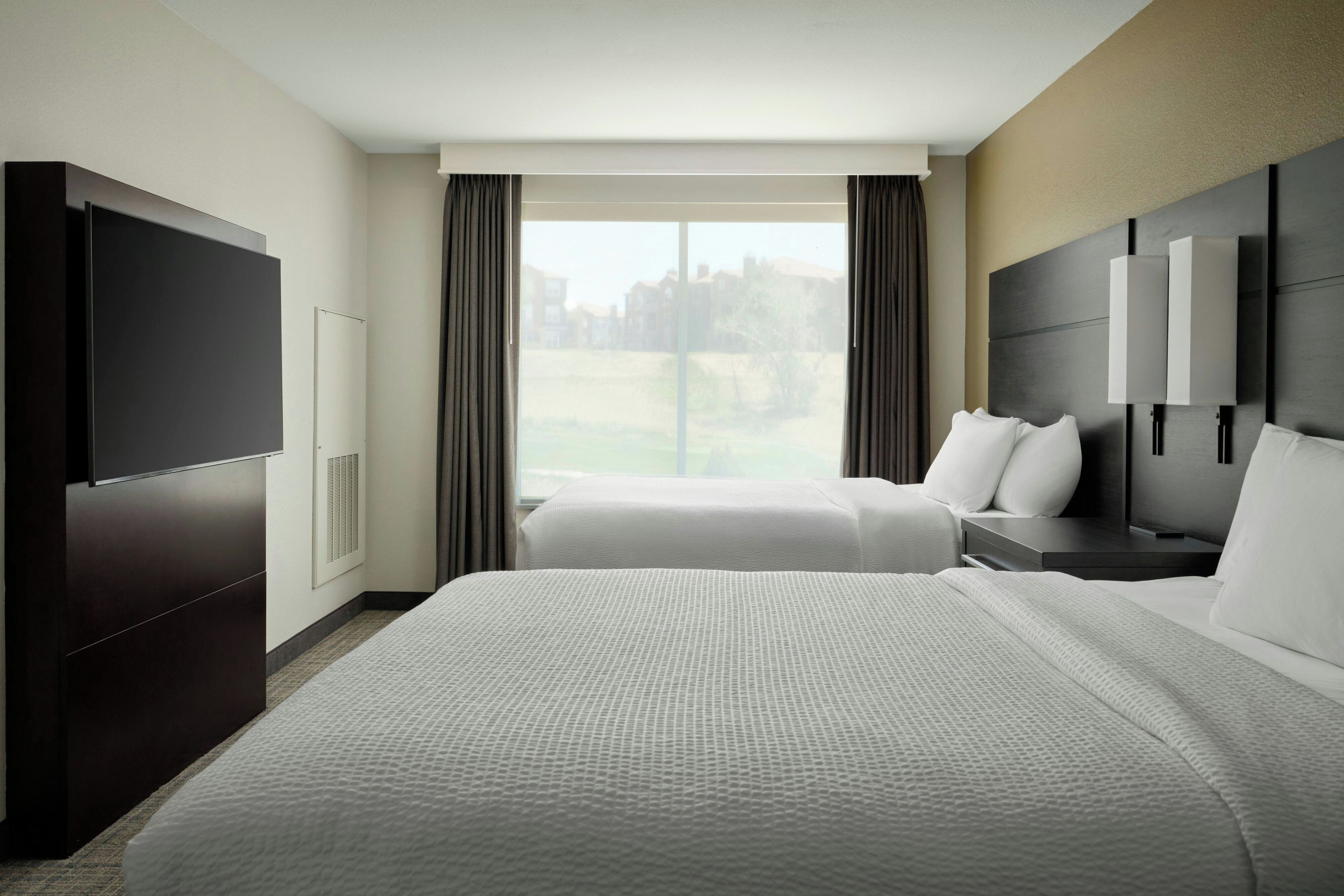 A hotel room with a large bed, a TV, a desk, and a window with curtains.