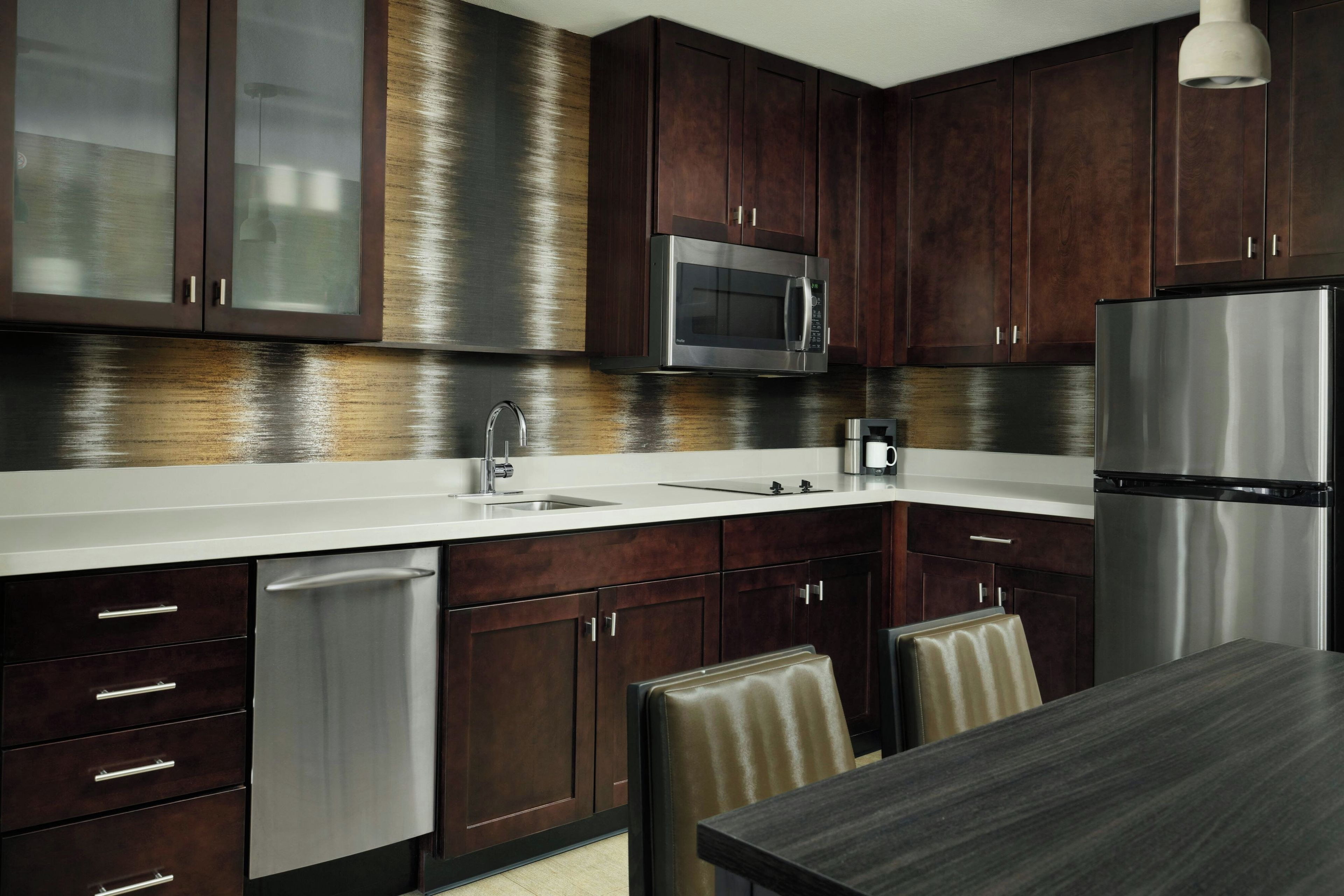 A modern kitchen with dark wood cabinets, stainless steel appliances, and a white countertop.