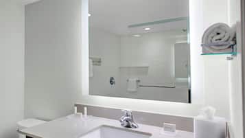Une salle de bain moderne avec un grand miroir, un lavabo blanc et une étagère en verre sur laquelle est posée une serviette enroulée.