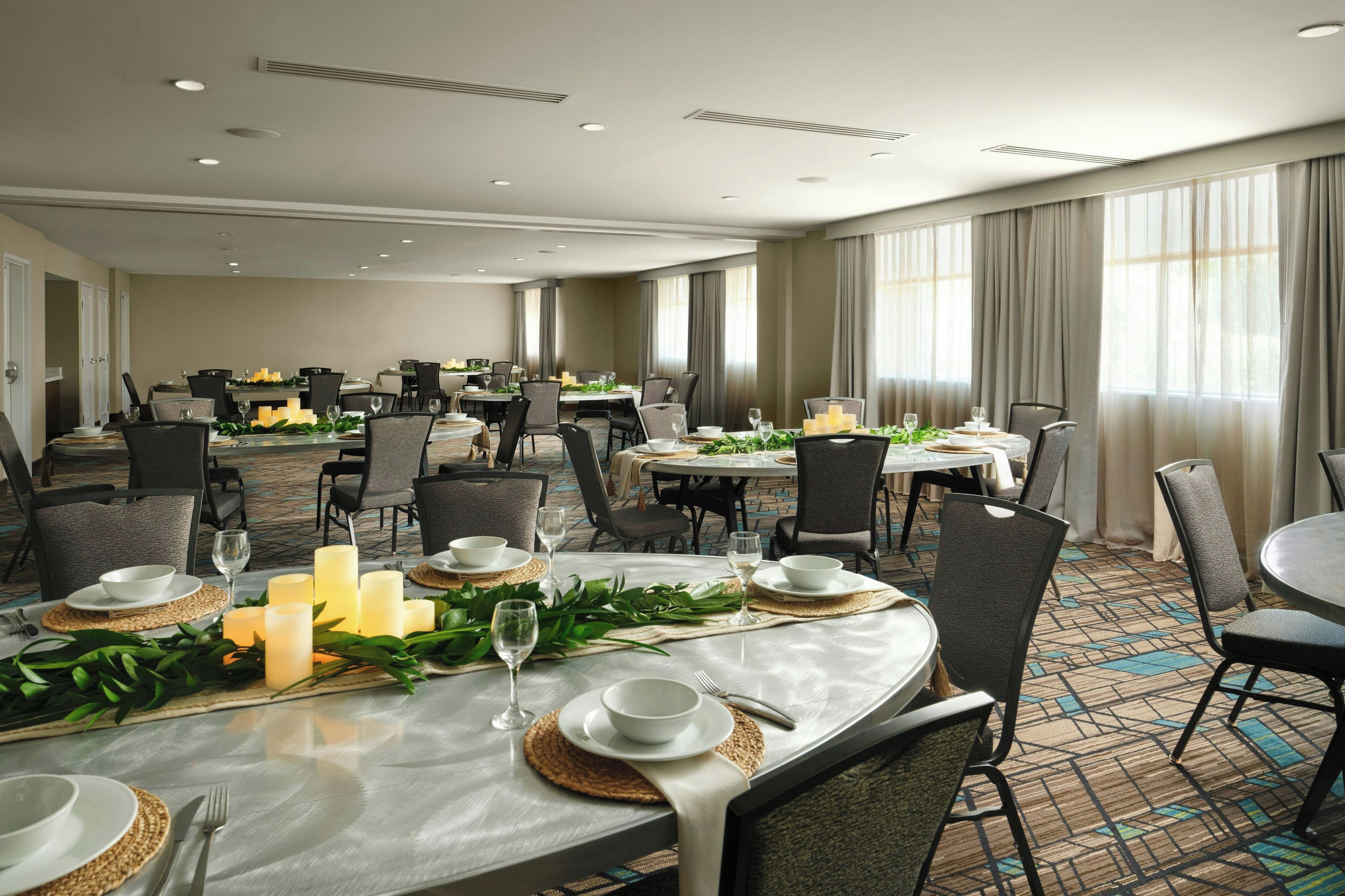 A hotel dining area with multiple tables set for dining, equipped with chairs, candles, and table settings.