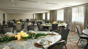 A hotel dining area with multiple tables set for dining, equipped with chairs, candles, and table settings.
