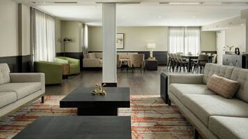 Une chambre d’hôtel moderne avec un canapé, un fauteuil vert, une table à manger avec des chaises et une grande fenêtre avec des rideaux.