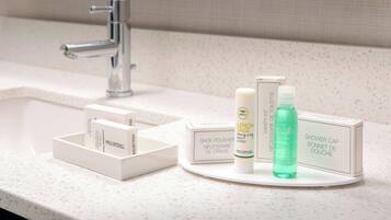 Un lavabo de salle de bain avec un robinet chromé, un plan de toilette blanc et un plateau contenant divers articles de toilette, notamment un pot de cirage à chaussures, une lotion pour le corps et un bonnet de douche.