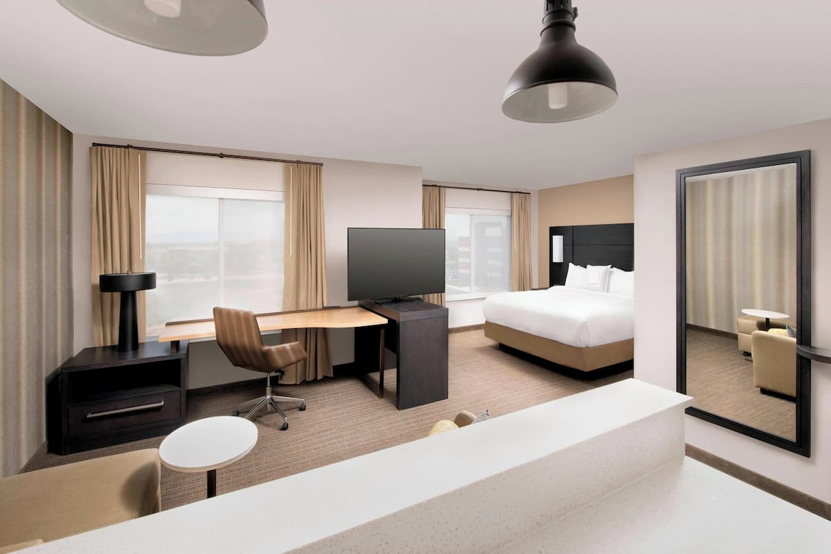 A hotel room with a bed, a desk with a chair, a television, a large mirror, and a small round table.