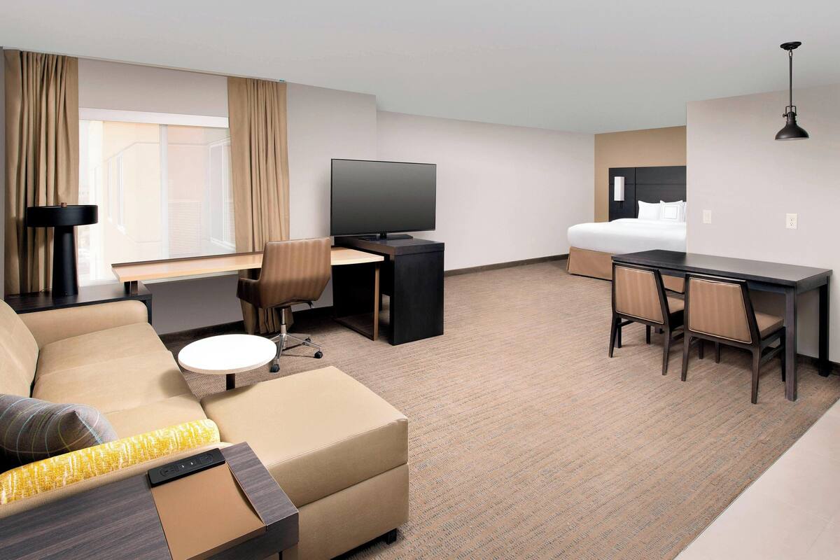 A hotel room with a sofa, a desk, a television, a bed, and a small table.