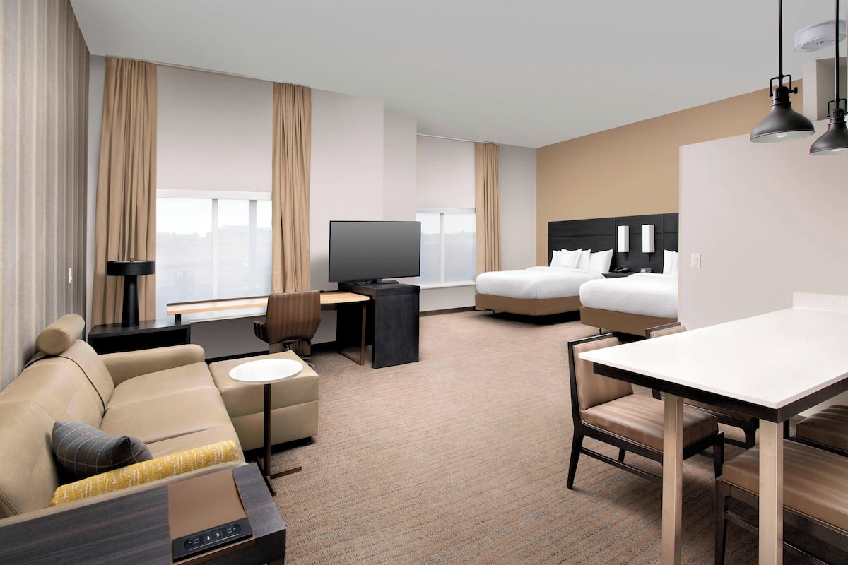 A hotel room with a sofa, a bed, a desk with a TV, and a dining table.