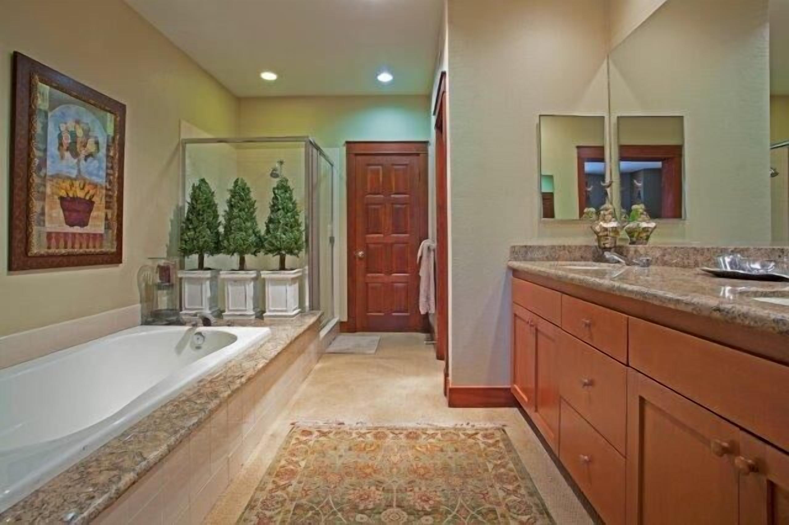 A bathroom with a large bathtub, a shower, and a sink. There are two Christmas trees and a door in the background.